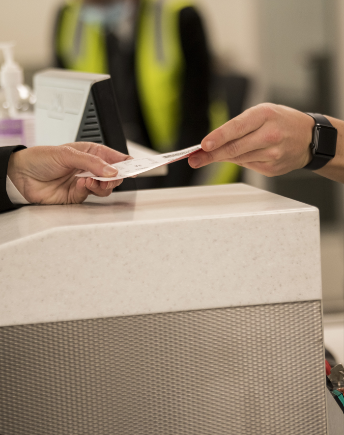 person handing boarding pass to staff member at airport counter