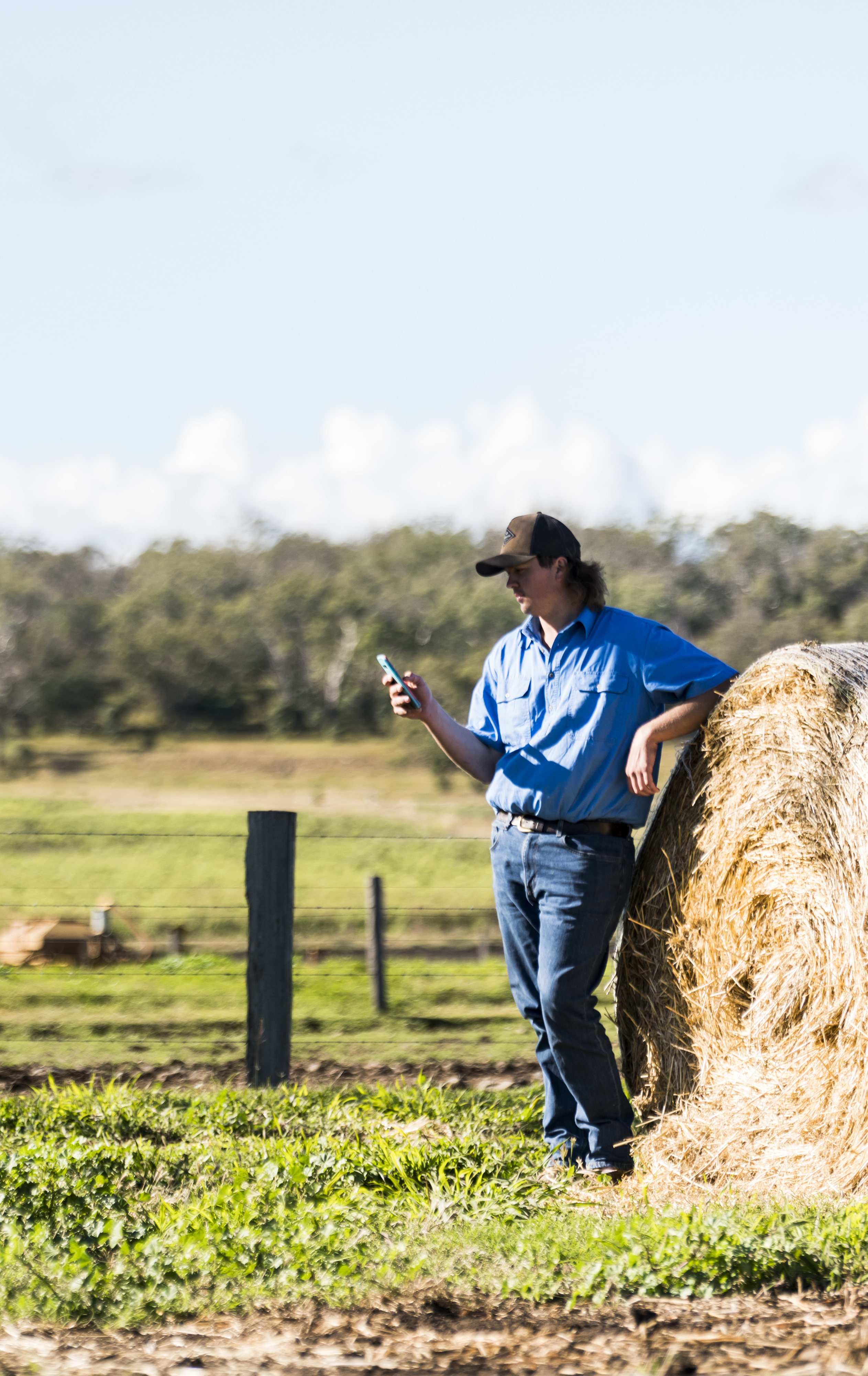 farmer leaning against haybale using phone