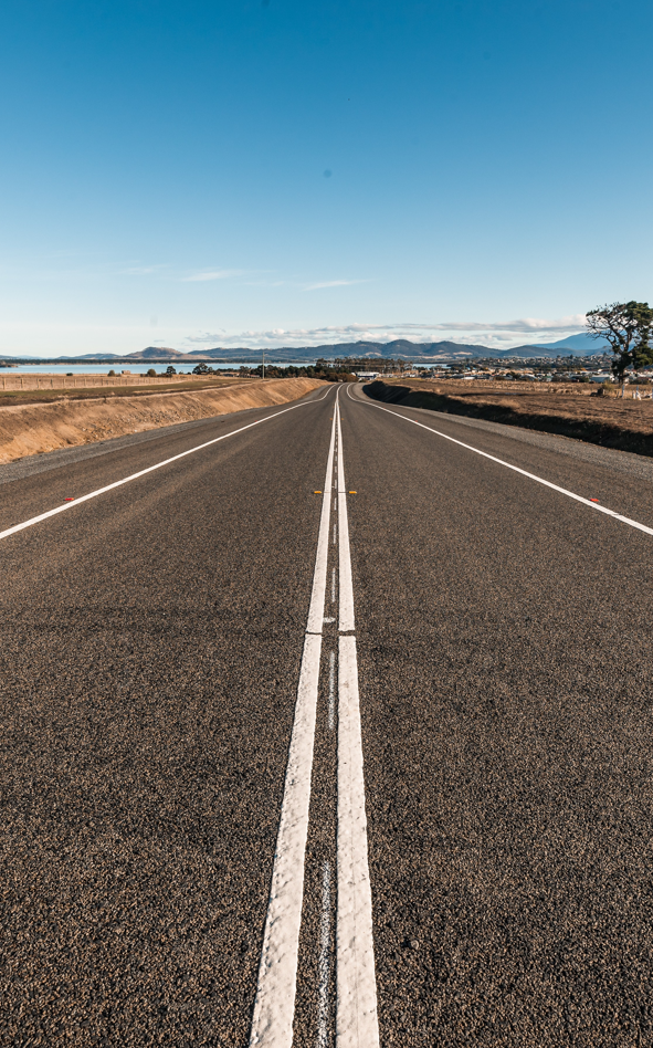 straight road disappearing into lake and hills on horizon 